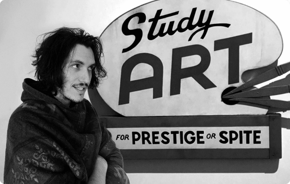Isaac Buckley in front of a hand-painted sign reading “Study Art for Prestige or Spite”